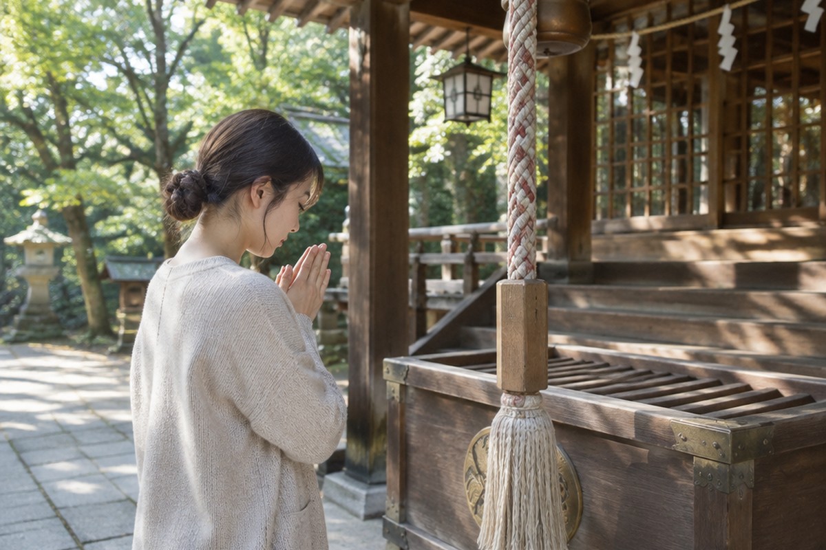 朝の神社で、静かに手を合わせる女性