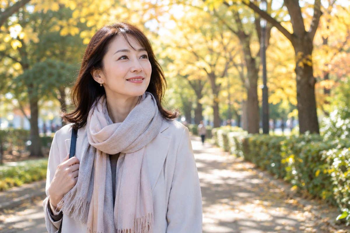 秋の朝、黄葉の並木道をおだやかな笑顔で歩く女性