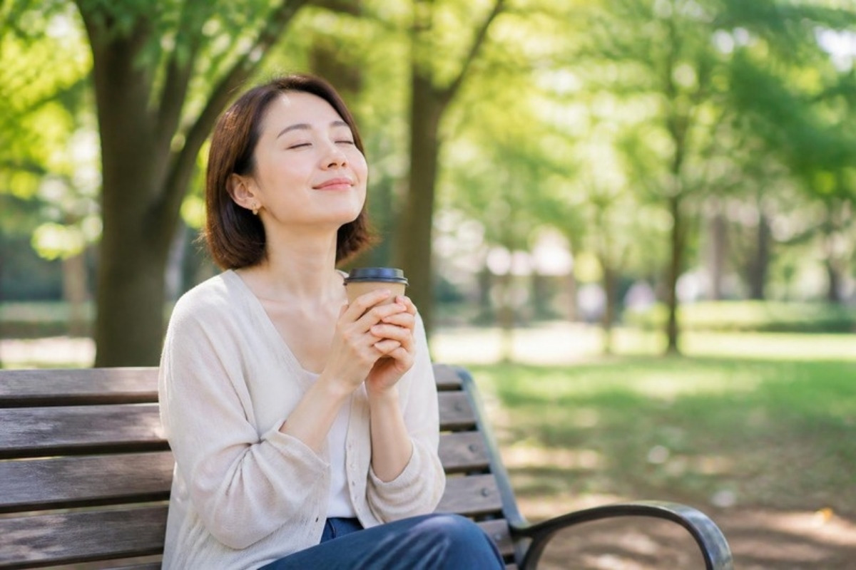 朝の公園のベンチで、コーヒーを手にひとりの時間を過ごす女性