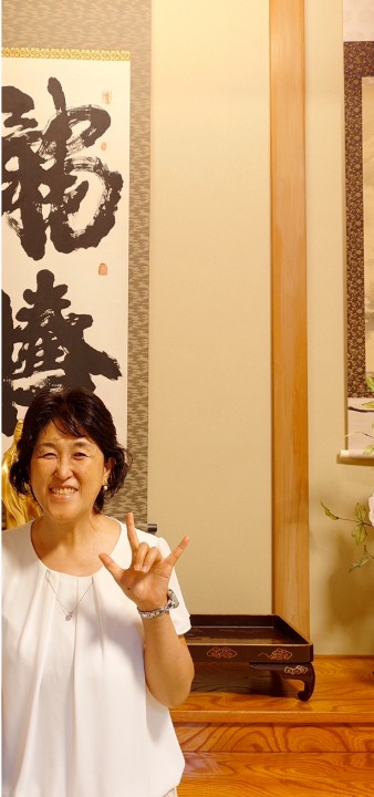 お寺でご住職から法話をうかがったあと、掛け軸の前でほほえむ愛原百麗
