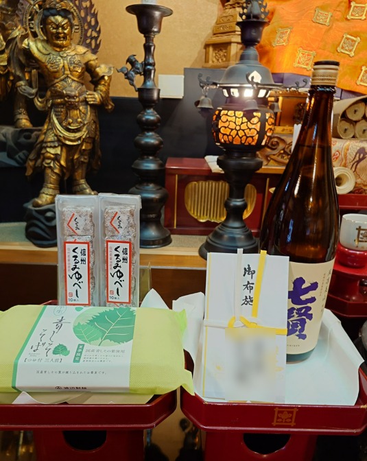 お寺のご本尊の前に供えた、お布施の封筒とお菓子、日本酒（封筒の名前はぼかしています）