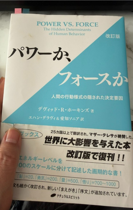 愛原百麗の手元にある『パワーか、フォースか 改訂版 人間の行動様式の隠された決定要因』（デヴィッド・R・ホーキンズ著、ナチュラルスピリット）