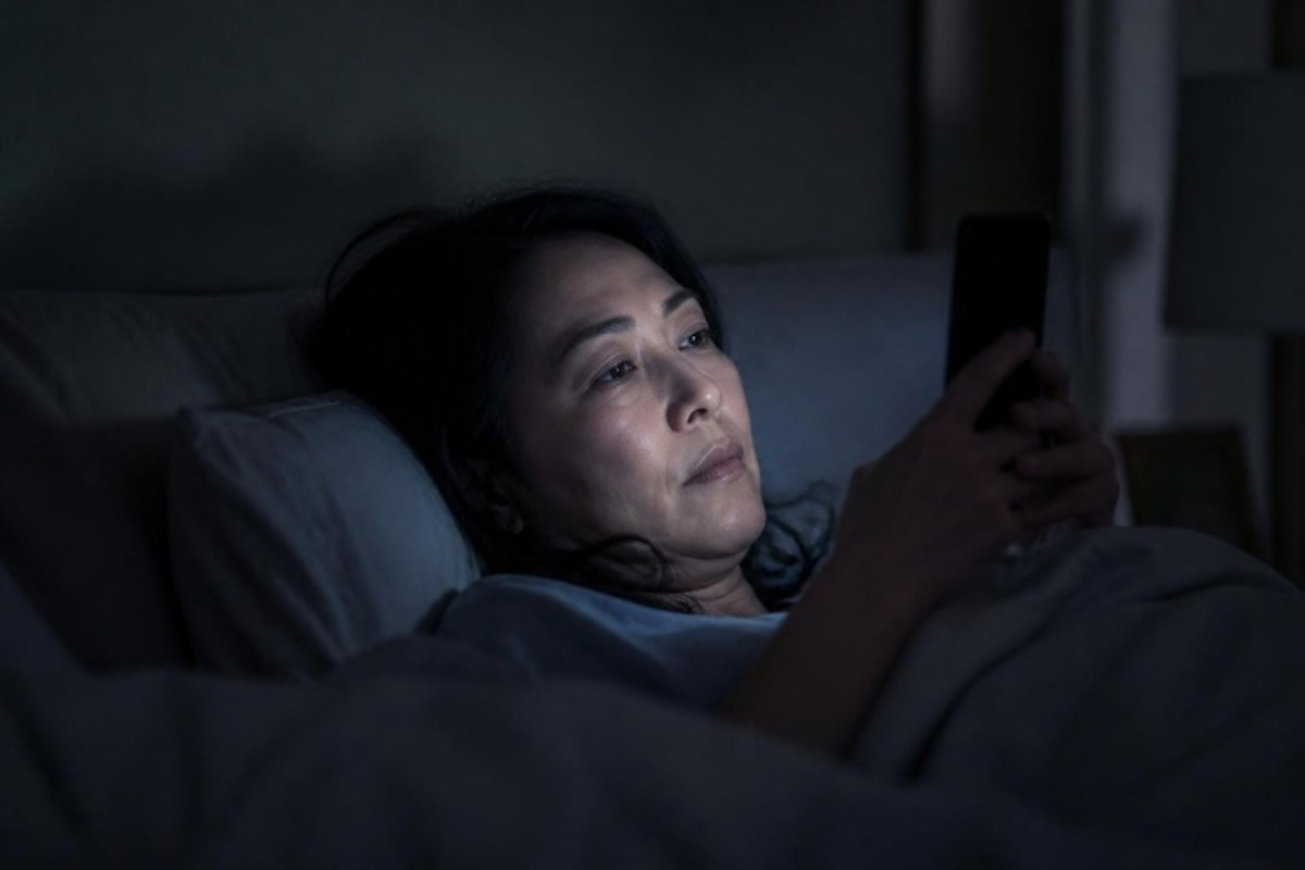 夜、ベッドでスマホのSNSを見つめる40代の女性
